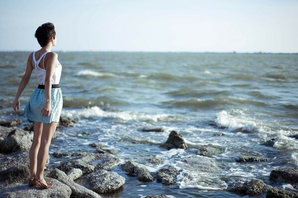 La ragazza sta con le spalle sulle pietre vicino alla riva del mare