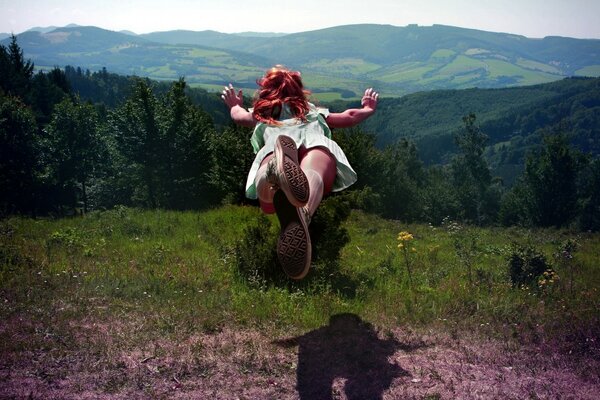 A girl jumps from a hill into the grass