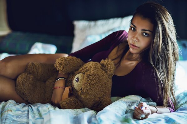 The girl is lying on the bed with a bear toy