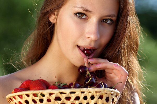 A girl with a basket of strawberries and cherries in her mouth