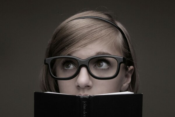 Fille avec des lunettes massives regarde par-dessus le livre