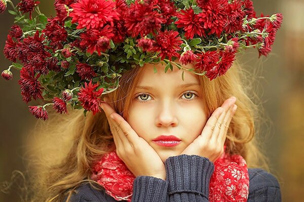 Hermosa niña en una corona de flores rojas