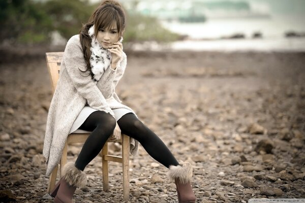 Chica en otoño junto al mar en una silla