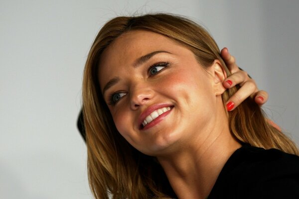 Model Miranda Kerr gracefully adjusts her hair with beautiful dimples on her cheeks