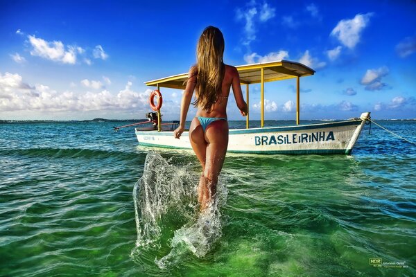 A girl walks across the sea to a boat in a bikini