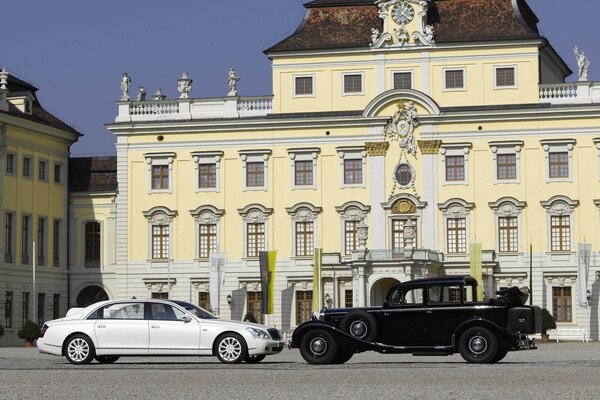 Белый майбах и черный автомобиль на фоне здания