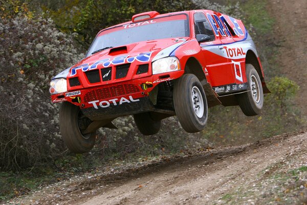 A red car is driving on a dirt road