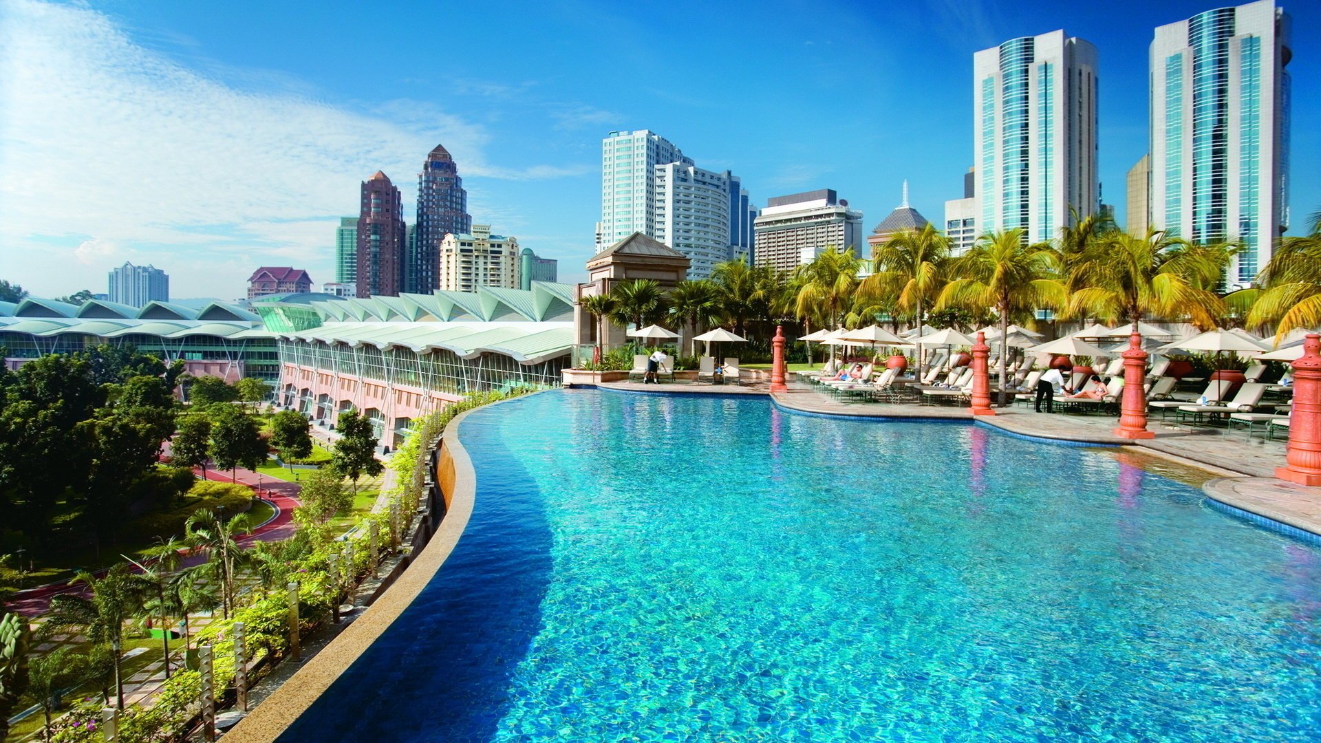 kuala lumpur blumen malaysia hotel schwimmbad wasser türkis palmen gebäude häuser stadt erholung himmel wolkenkratzer tag sonniger tag vegetation grün sonnenschirme liegestühle bäume