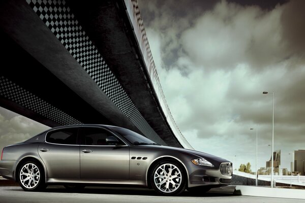 Coche Maserati plateado debajo del puente, cielo gris