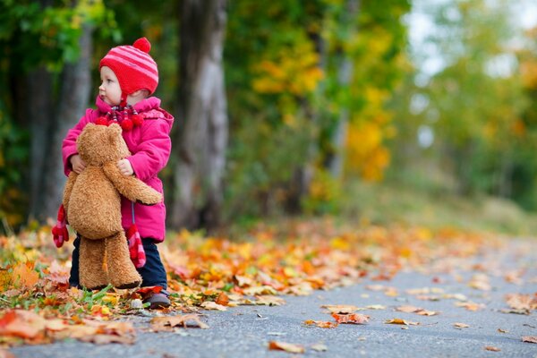 A child with a bear stands in autumn