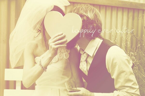 Les jeunes mariés ont couvert leur baiser avec un cœur en carton