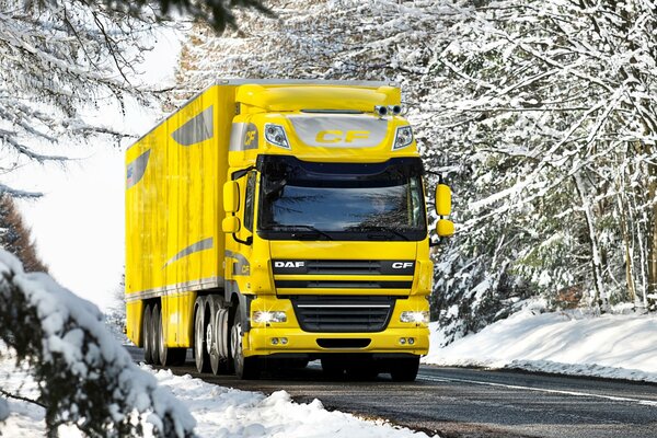Zimą żółta ciężarówka jedzie po zaśnieżonej drodze
