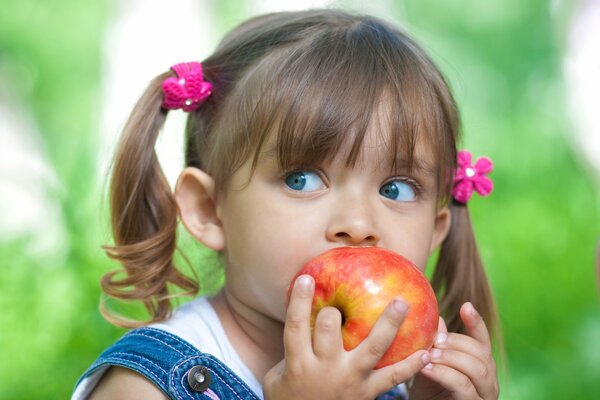 Niña de ojos azules come una manzana