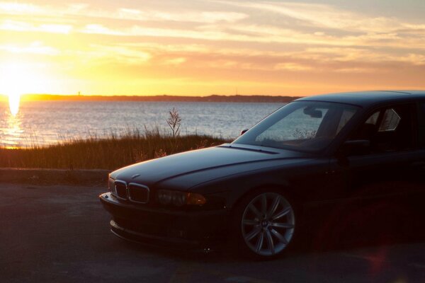 Bmw standing on the embankment by the water against the background of the departing sun