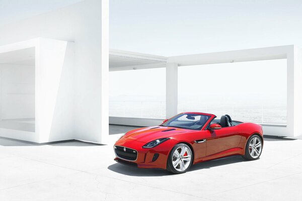 A red sports car stands against the background of a white structure