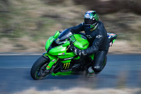 A motorcyclist wearing a helmet on a green kawasaki enters a turn