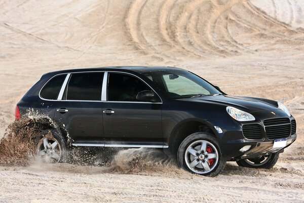Schwarzer Porsche Cayenne fährt in der Wüste über den Sand