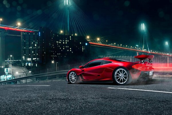 Un McLaren rojo corre por el puente a la luz de las luces nocturnas. Un automóvil deportivo caro vuela por el puente nocturno