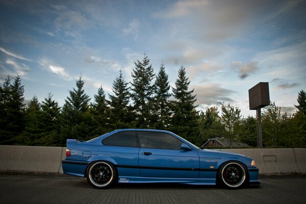 BMW E36 sintonizzata blu su sfondo foresta