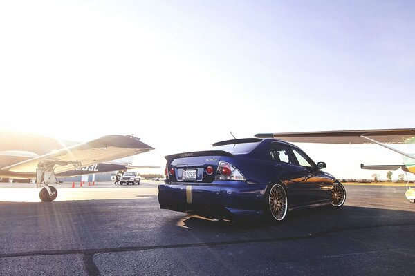 Dark blue Lexus at the airfield with several planes