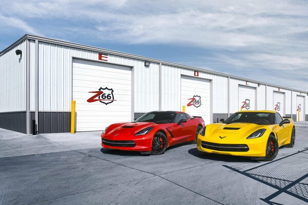 Jasne samochody sportowe na tle garaży pod błękitnym niebem. Czerwony i żółty Chevrolet Corvette w pobliżu garaży