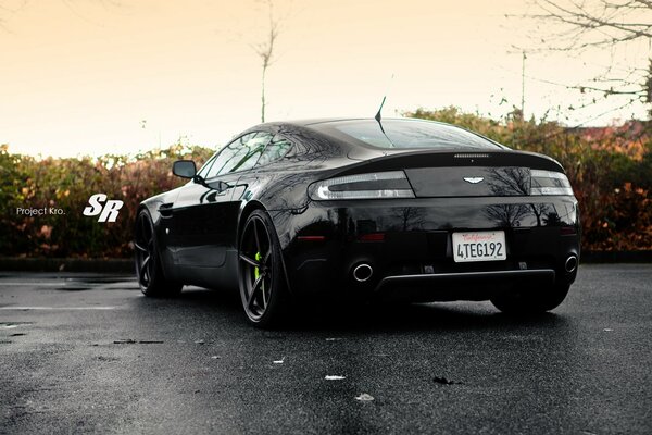 El coche negro de Aston Martin. Asfalto húmedo con cielo al atardecer
