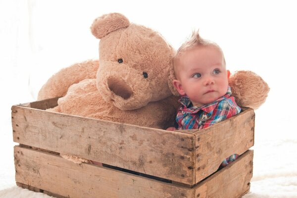 Un niño con un osito de peluche en una Caja de madera