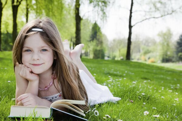 Una niña con un libro yace en el césped