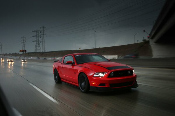 Auto rossa Ford Mustang sulla strada contro il cielo tempestoso