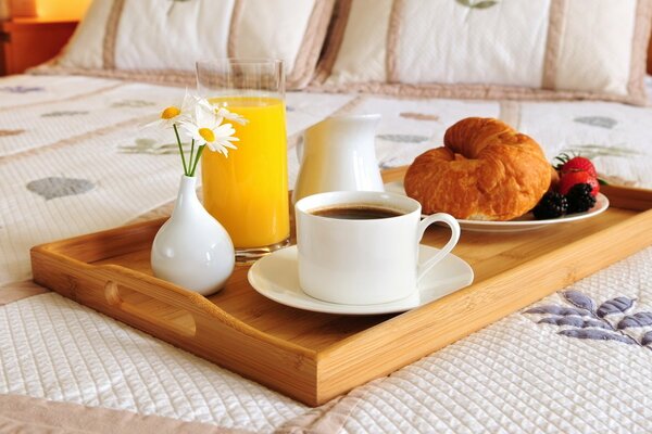 Ein Glas Orangensaft, eine Tasse Tee und ein Stand auf einem Tablett auf dem Bett