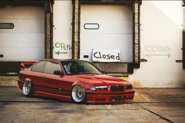 Rojo tuneado BMW e 36 en el estacionamiento. cerca del almacén