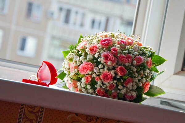 Wedding bouquet of roses and wedding rings in a box on the windowsill