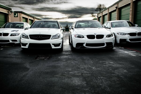 3 white BMWs and 1 white Mercedes on the background of garages