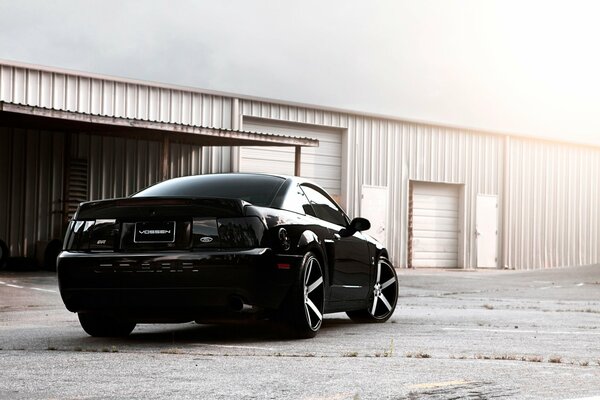 Schwarzer Ford Mustang auf Hangar-Hintergrund