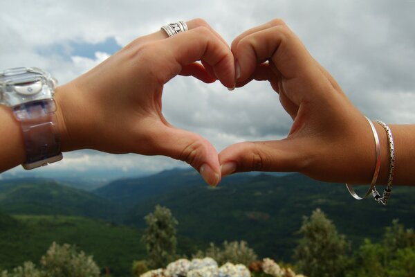 Corazón con las manos en el fondo de las montañas