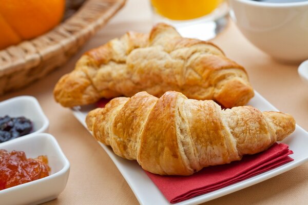 Ein Paar Croissants auf einer Serviette mit nebeneinander stehenden Untertassen mit Marmelade