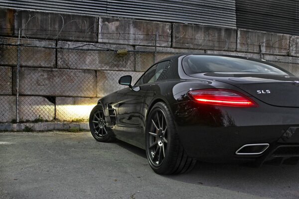 Mercedes benz sls amg stands against a wall of concrete blocks with the headlights on