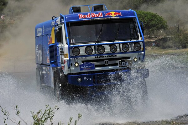 Blue KAMAZ rides on the water, splashes scatter on the sides of the MERCEDES