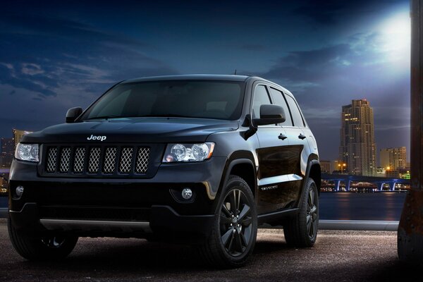 Voiture jeep grand cherokee dans la nuit sur le fond de la ville et la lune brille