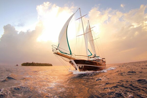 A ship with white sails on a sunset background