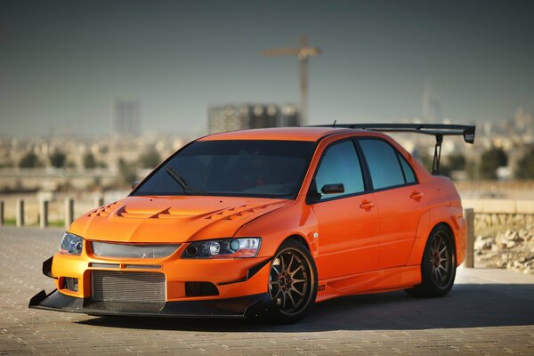 Mitsubishi Lancer naranja en el fondo de la ciudad