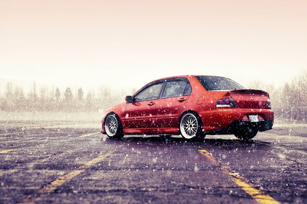 Orange Mitsubishi lancer evolution in winter. Snow is falling