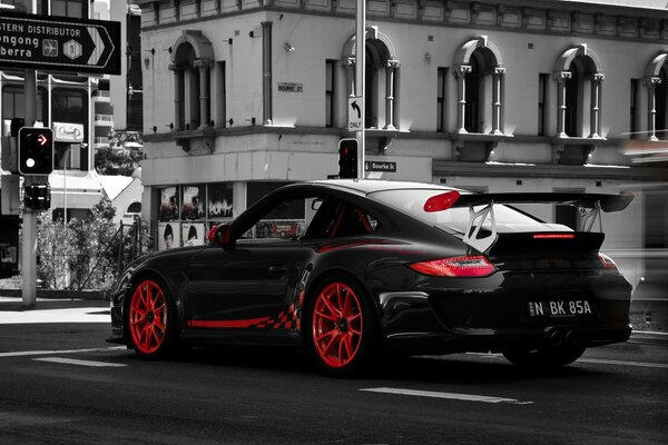 Black Porsche with red wheels at a city intersection