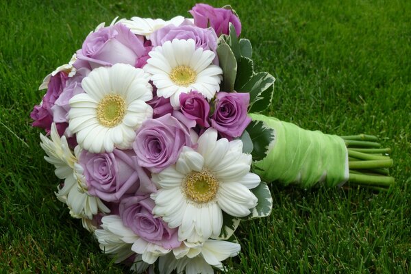 A bouquet of chamomile and roses lies on the grass