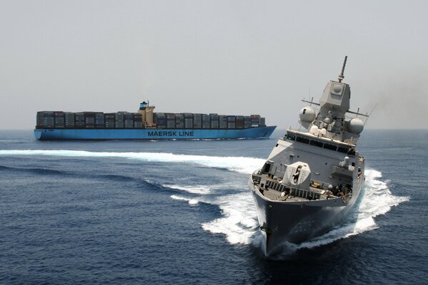 Maneuvering military frigate at sea against the background of a container ship