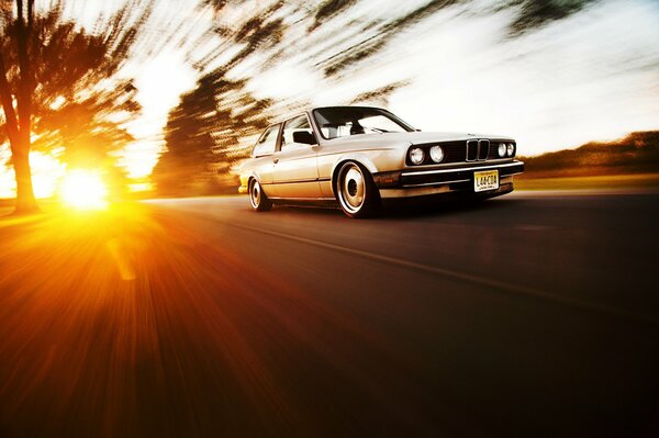 Silver BMW e30 coupe rushes along the road away from the sun