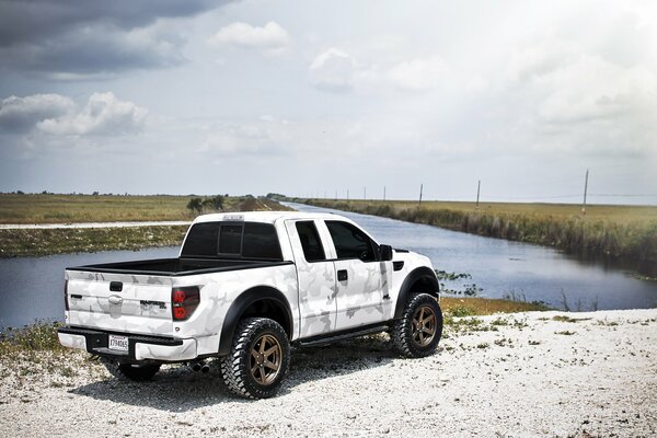 White pickup truck by the river under a cloudy sky