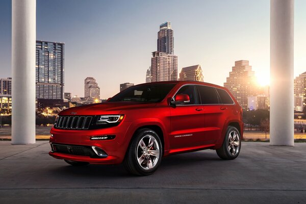 A red jeep stands against the background of the city at sunset