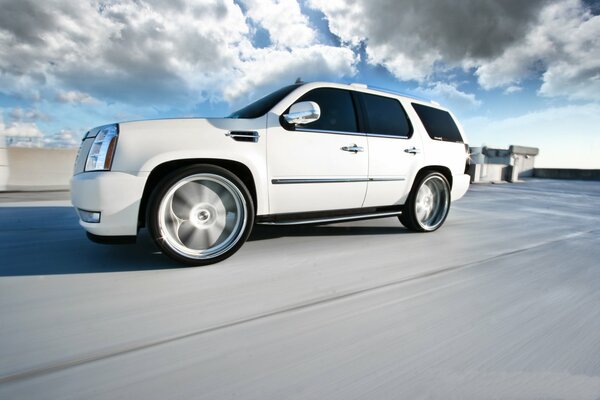 The white cadillac escalade is going fast, it has blurry hubcaps on the wheels