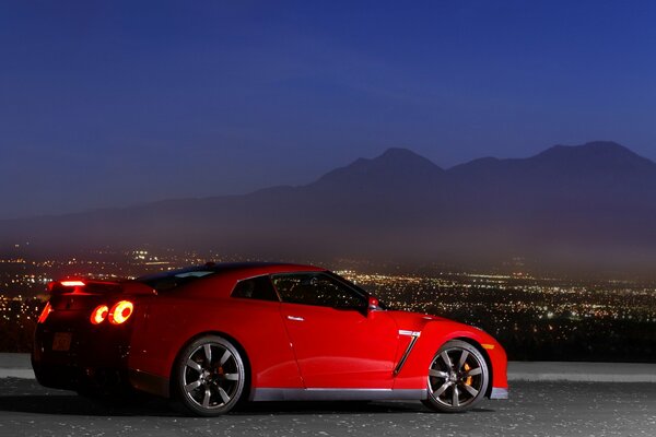 A red Nissan stands in profile against the background of the evening city